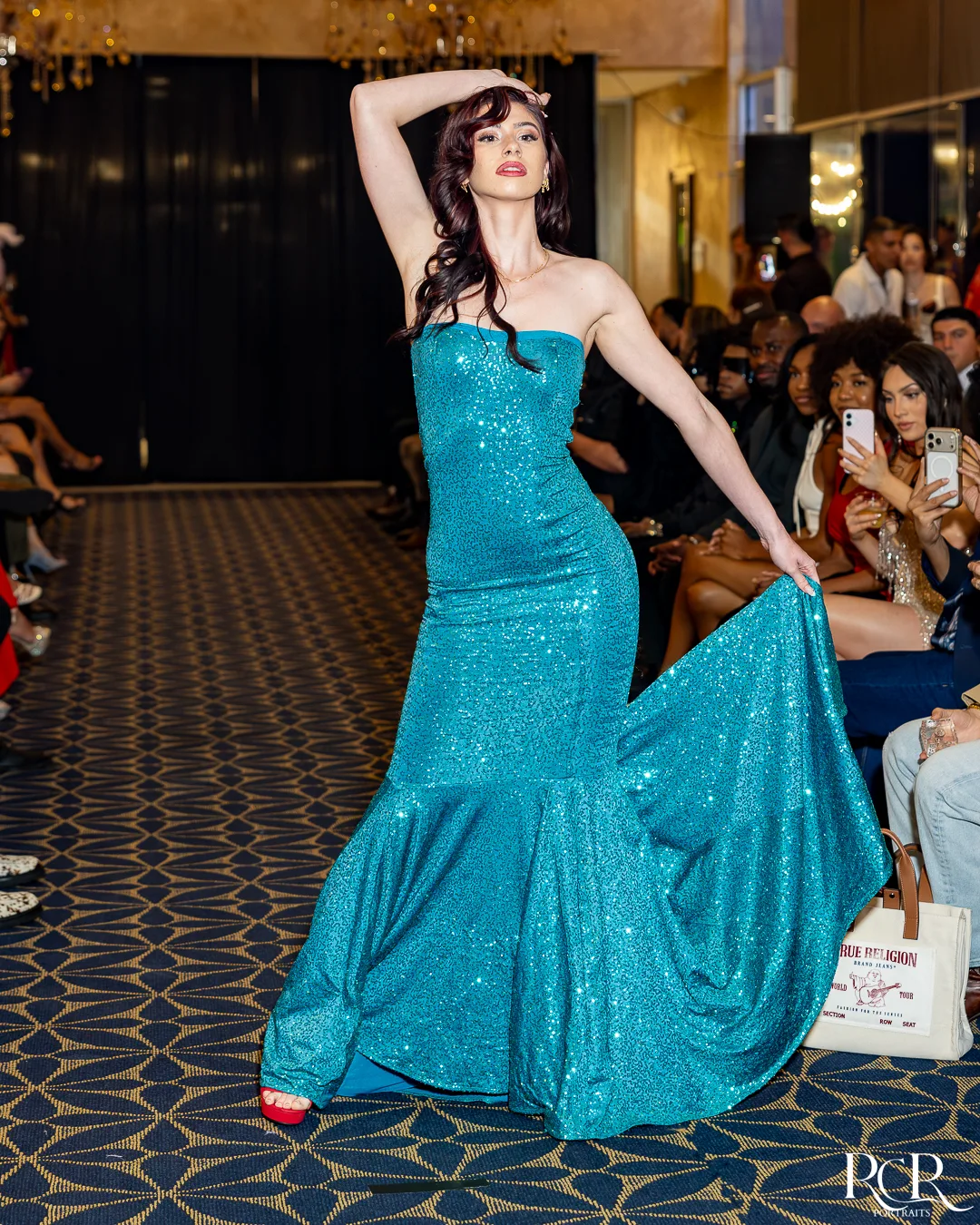 Model walking between seated guests in a teal gown at The Gatsby Affair