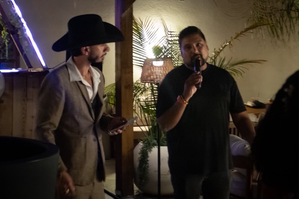 Nabeel speaking into a microphone beside a cowboy-hatted guest at Old Money