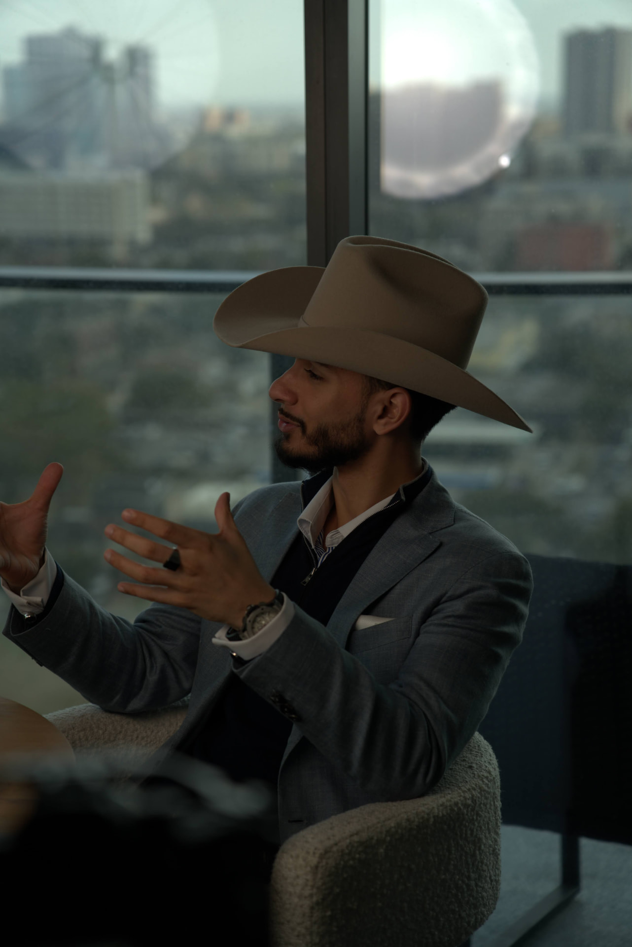 Cowboy-hatted podcast participant gesturing beside a microphone and a Houston skyline window